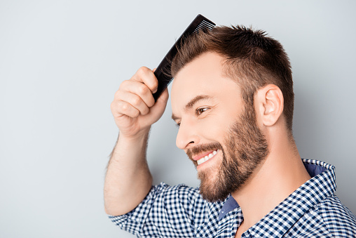 Portrait of handsome cheerful young man combing his hair