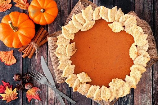Thanksgiving pumpkin pie with autumn leaf pastry design, overhead scene on rustic wood