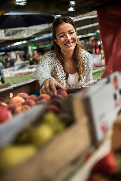 istock Young smiling woman choosing fresh peaches on farmer's market. 607258564
