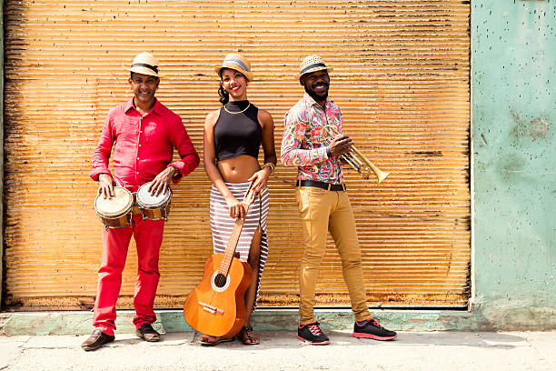 Cuban Musical Trio Cuban musical band, the trio consisting of a well known musicians standing against a yellow closed shop shutter. Beautiful young woman standing in the middle, holding a guitar. The man on the left holding the small drums bongos, and a musician on the left holding a trumpet. Havana, Cuba rumba photos stock pictures, royalty-free photos & images