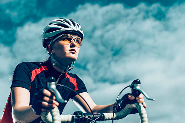 Professional female bike rider rides bicycle Close up of female cyclist who rides a professional bicycle. The cyclist wears sports clothes and a helmet. It is summer and the sun shines. forward athlete stock pictures, royalty-free photos & images