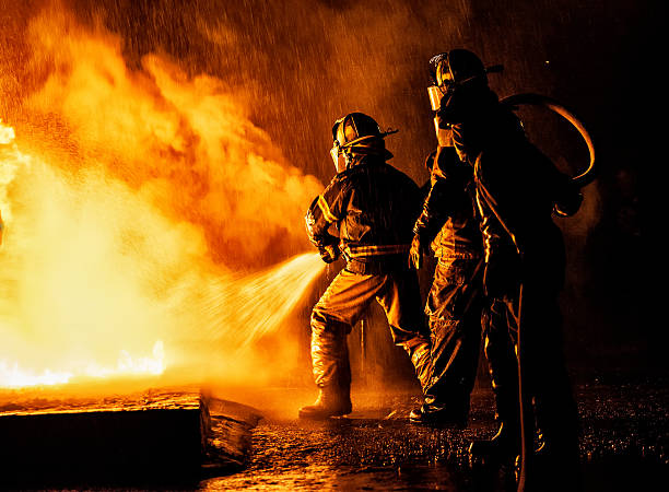 due vigili del fuoco che combattono un incendio con un tubo e acqua - vigile del fuoco foto e immagini stock