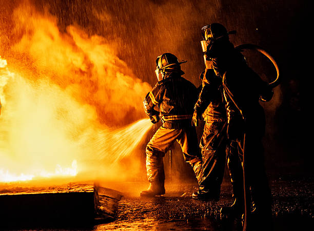 two firefighters fighting a fire with a hose and water - brandweer stockfoto's en -beelden