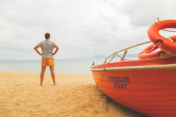 Lifeguard posing with his boat on the beach. Focus is on the boat.
