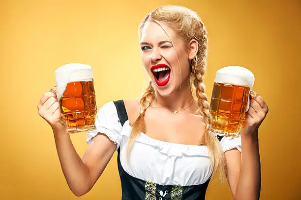 Half-length portrait of young sexy blonde with big breast wearing black dirndl with white blouse holding the beer mug Isolated on dark background