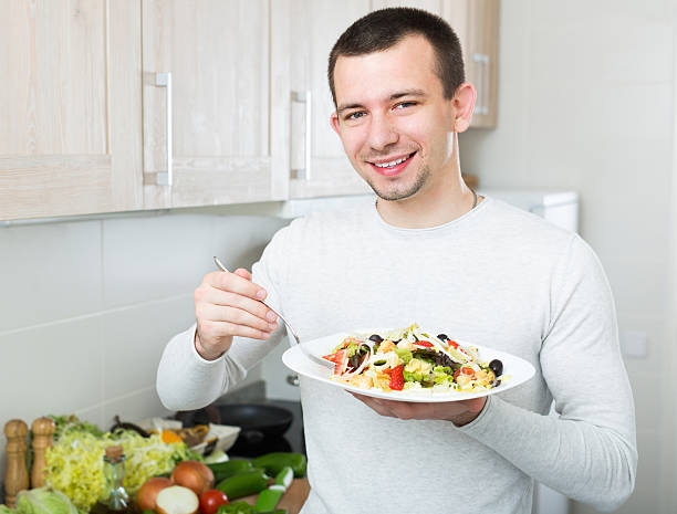 istock Man eating vegetable salad in kitchen 607275804