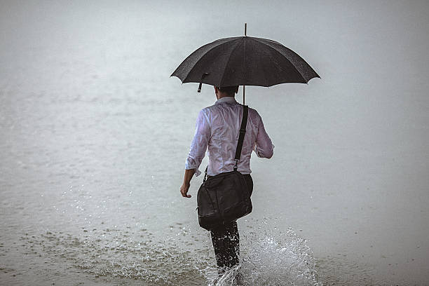 istock Handsome man holding umbrella walks through the water during rain 607279050