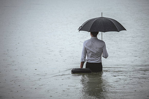 istock Handsome man standing in water and holding umbrella during rain 607279476