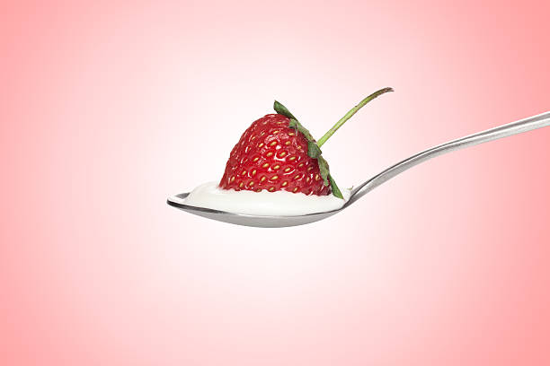 istock White cream and a strawberry in silver spoon on pink 607279838