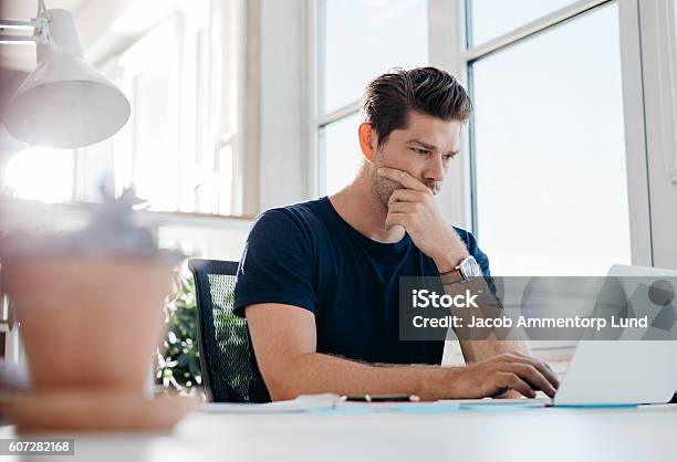 Pensativo Joven Ejecutivo Masculino Usando La Computadora Portátil En Su Escritorio Foto de stock y más banco de imágenes de Concentración