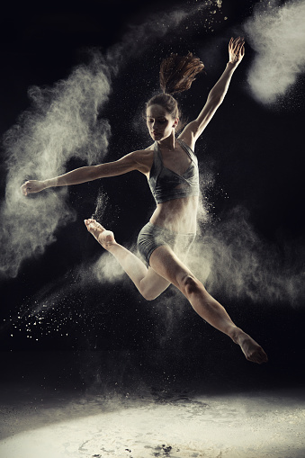 Young woman dancing, turning around and splashing powder everywhere around her. She is ballerina and looks very attractive