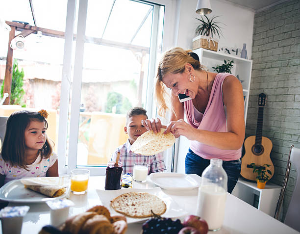 Busy Mother Organizing Children At Breakfast In Kitchen