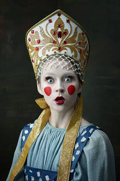 The surprised girl posing in Russian traditional costume. Woman is wearing sarafan and kokoshnik on black.