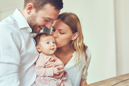 Smiling mother and father holding their newborn baby daughter at home