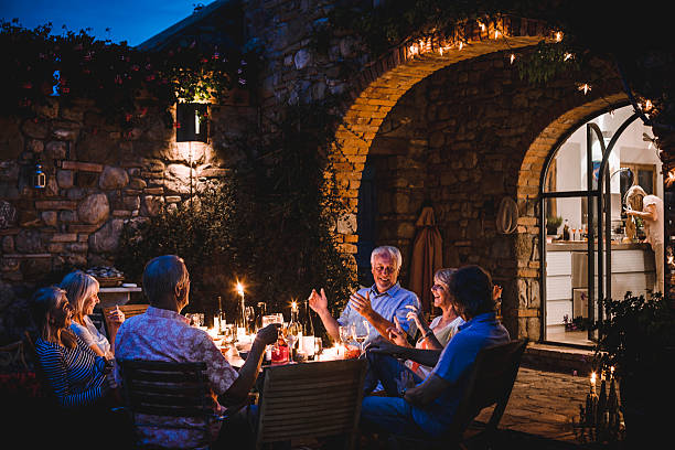 Alfresco Dining in the Evening A group of mature friends are sitting around an outdoor dining table, eating and drinking. They are all talking happily and enjoying each others company as darkness falls. The image has been taken in Tuscany, Italy. candle light dinner stock pictures, royalty-free photos & images