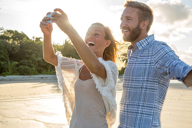 istock Beautiful young couple take selfie on beach using mobile phone 607296514