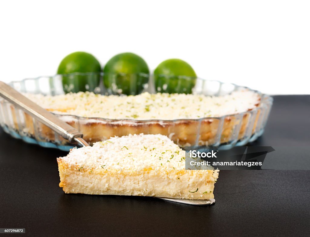 Lemon Lime Impossible Pie Slice on a Silver Pie Server Lemon, lime, coconut impossible pie with white chocolate shavings slice on a silver cake server with limes and dish in the background Lemon - Fruit Stock Photo