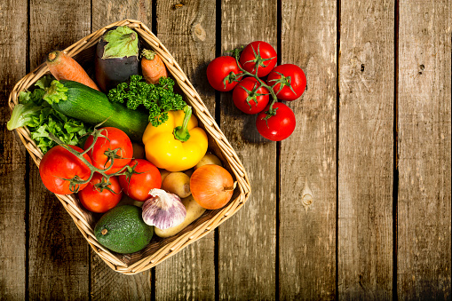 View directly above of a bunch of fresh vegetables in a basket and sitting on a weathered wooden table. Studio shot and plenty of copy space.