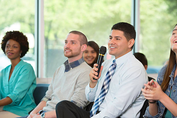 istock Mid adult Hispanic man asks question at town hall meeting 607459948