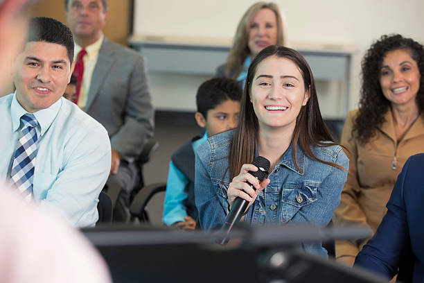 istock Young Hispanic woman asks question during town hall meeting 607460326