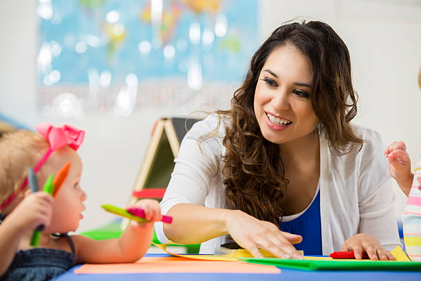 istock Beautiful daycare teacher helps toddler with coloring project 607460582