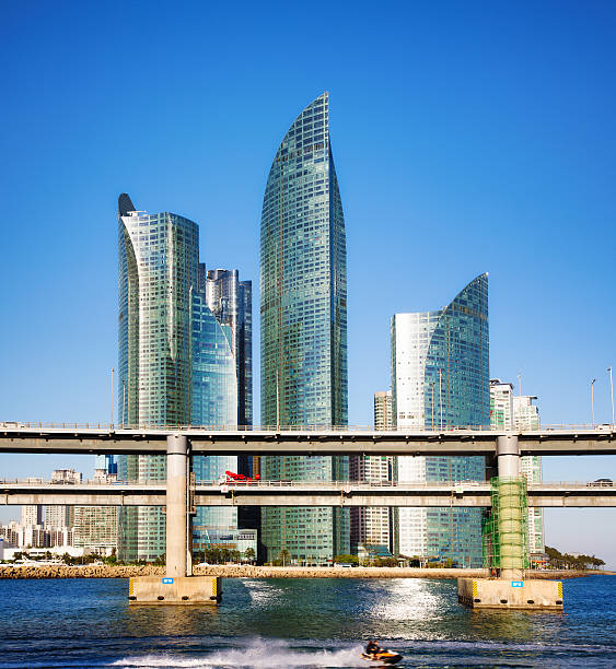 Busan South Korea modern skyscrapers with access ramps to the Gwangandaegyo Bridge in front of them.  A fast moving defocused couple on jetski is at the very bottom.