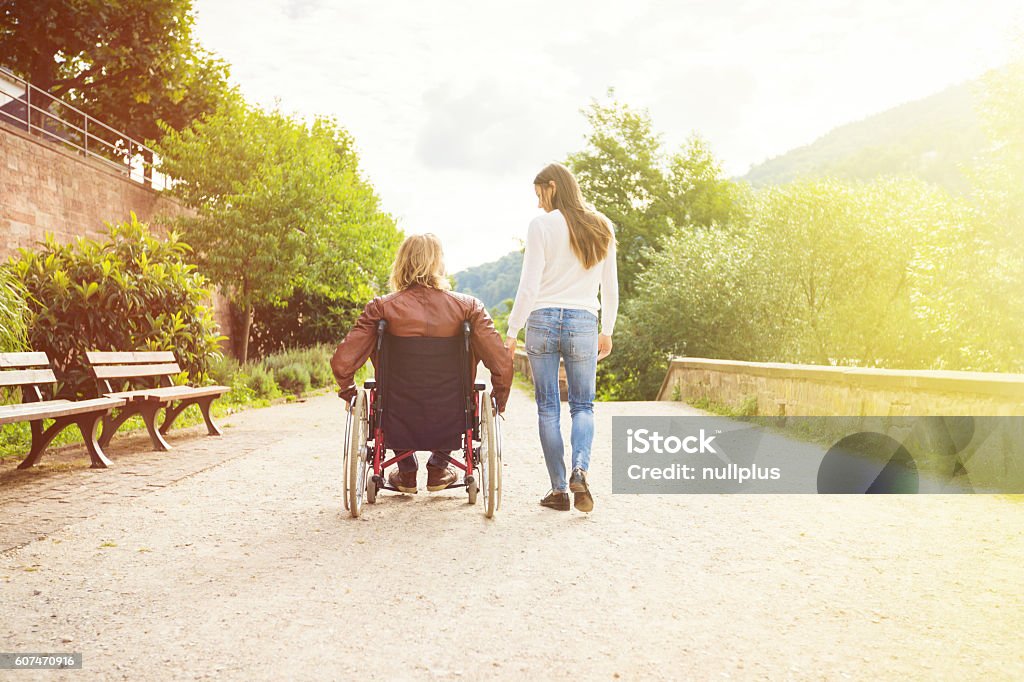 Pareja joven en silla de ruedas paseando por el parque - Foto de stock de Silla de ruedas libre de derechos