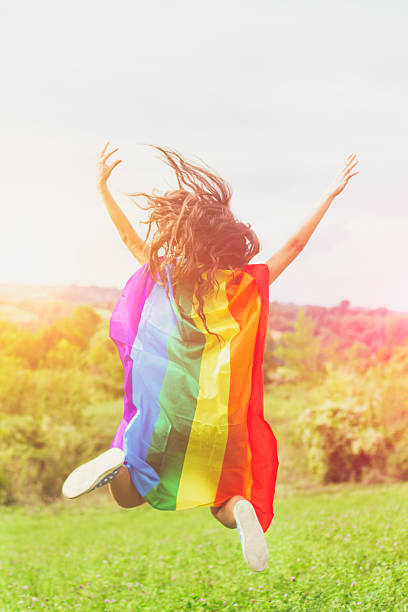 mujer con la bandera del arco iris que salta en la naturaleza - lesbian gay man rainbow multi colored fotografías e imágenes de stock