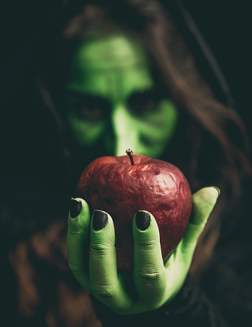 Witch green hand holding a rotten red apple. Shallow depth of field.