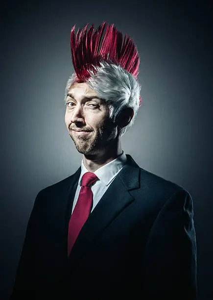 A business person in punk rock style sports a large pink and white mohawk with a matching pink tie.  A humorous and ironic culture clash portrait of youth style and business wear.  Vertical studio portrait.