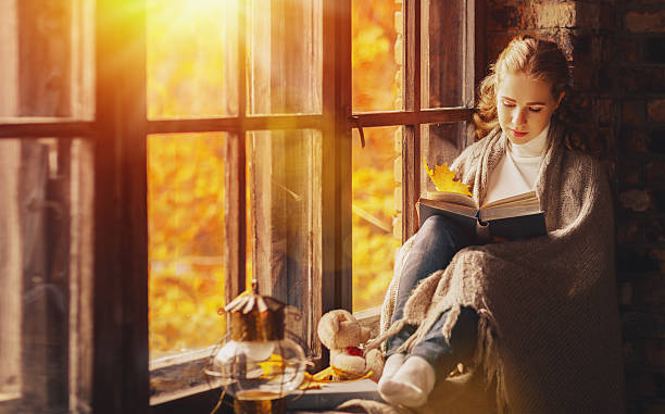 istock Happy young woman reading book by window in fall 607482164