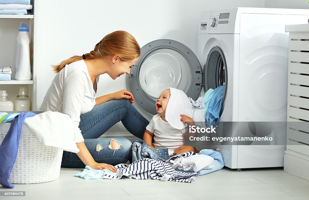 mother a housewife with a baby  fold clothes mother a housewife with a baby engaged in laundry fold clothes into the washing machine Mother Stock Photo