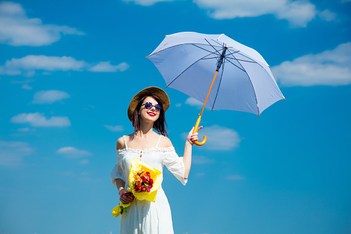 photo of the beautiful young woman with bouquet and umbrella on the sky background