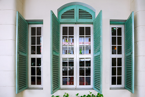 Old window with green shutters against the white walls.