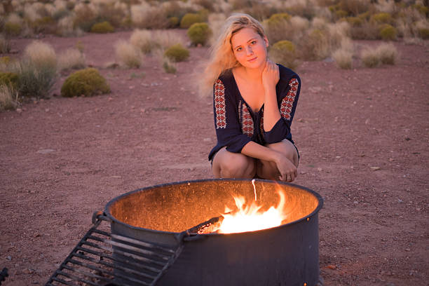 блондинка молодая женщина сидит у костра яму - fire pit fire camping campfire стоковые фото и изображения