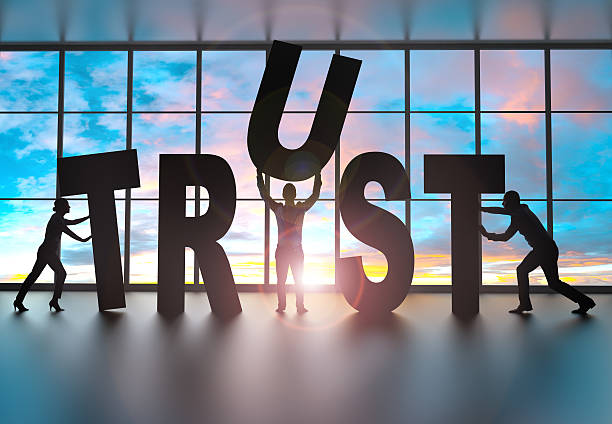 Team building the word trust silhouettes of business partners moving letters inside an office at sunset. They are building the word trust trust stock pictures, royalty-free photos & images