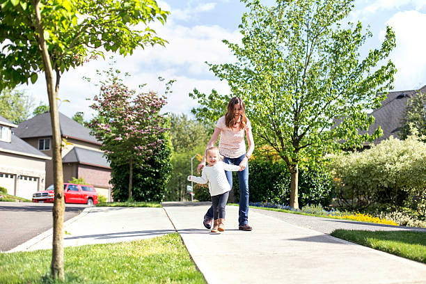 istock Young mother helps her daughter walk down the sidewalk 607497992