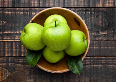 Green organic healthy apples in bowl on wooden board. Healthy food