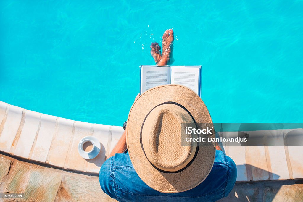 photo of a man reading a book photo of a man reading a book next to the swimming pool,relaxing,sitting on the edge with his legs in the water Reading Stock Photo