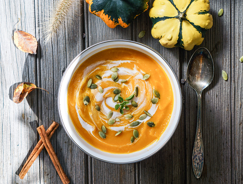 Roasted pumpkin soup with cream and pumpkin seeds on wooden background.