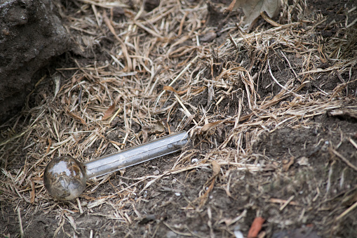 A used and discarded crack pipe on the ground, with dirt, rocks, and dead grass