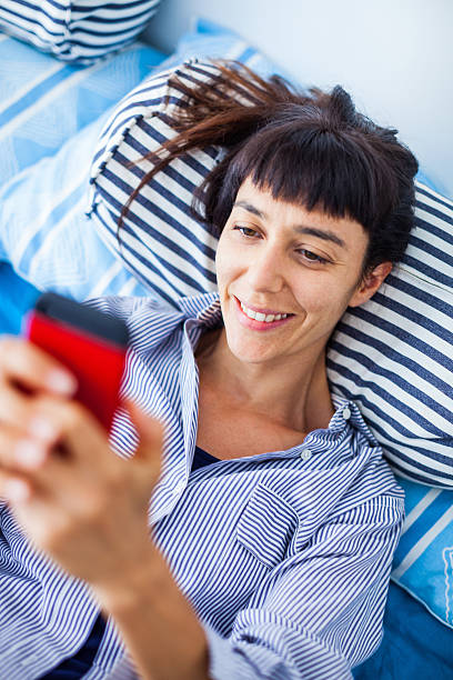 donna che telefona al telefono sdraiata sul letto - italian culture women looking at camera cheerful foto e immagini stock