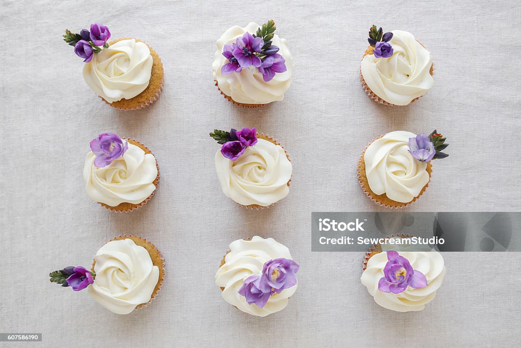 Schlagsahne frostende Vanille Cupcakes mit lila essbaren Flowe - Lizenzfrei Cupcake Stock-Foto