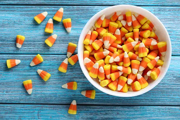 Photo of Halloween candy corns in bowl on blue wooden background