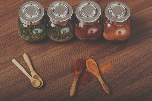 Four glass jar with spices and four wooden spoon on the table.
