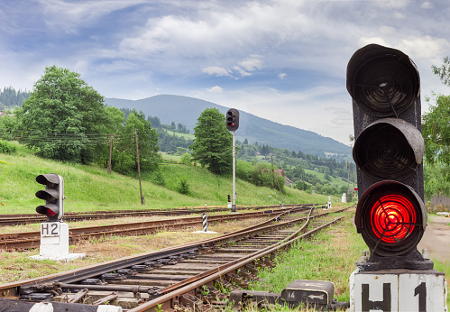Railroad tracks and other railway equipment with traffic light glows red on the foreground on the provincial railway station in the Carpathians at summer evening