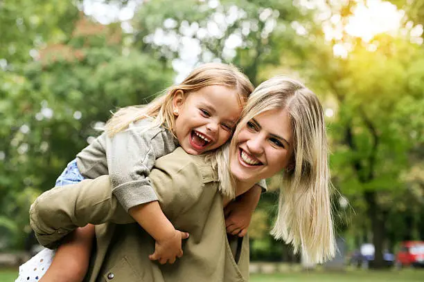 Cute young daughter on a piggy back ride with her mother.