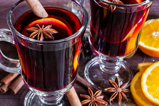 two glasses of hot mulled wine with spices and sliced orange on wooden background. close up