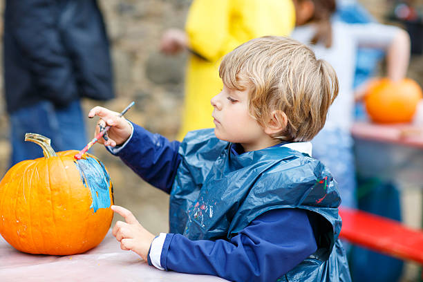 istock Little kid boy painting with colors on pumpkin 607608770