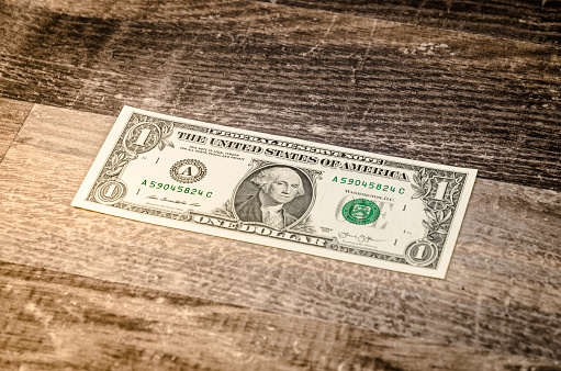 Photo of a US Dollar bill on a rustic old vintage hardwood table. Strong colors and high contrast.